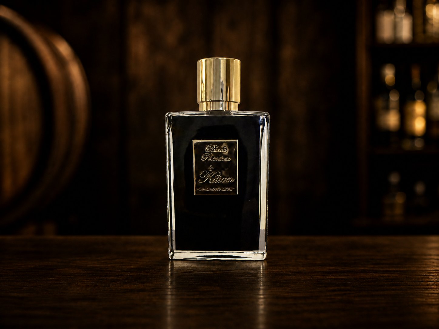 Kilian Black Phantom perfume bottle on a dark bar top, an oak barrel softly out of focus behind it