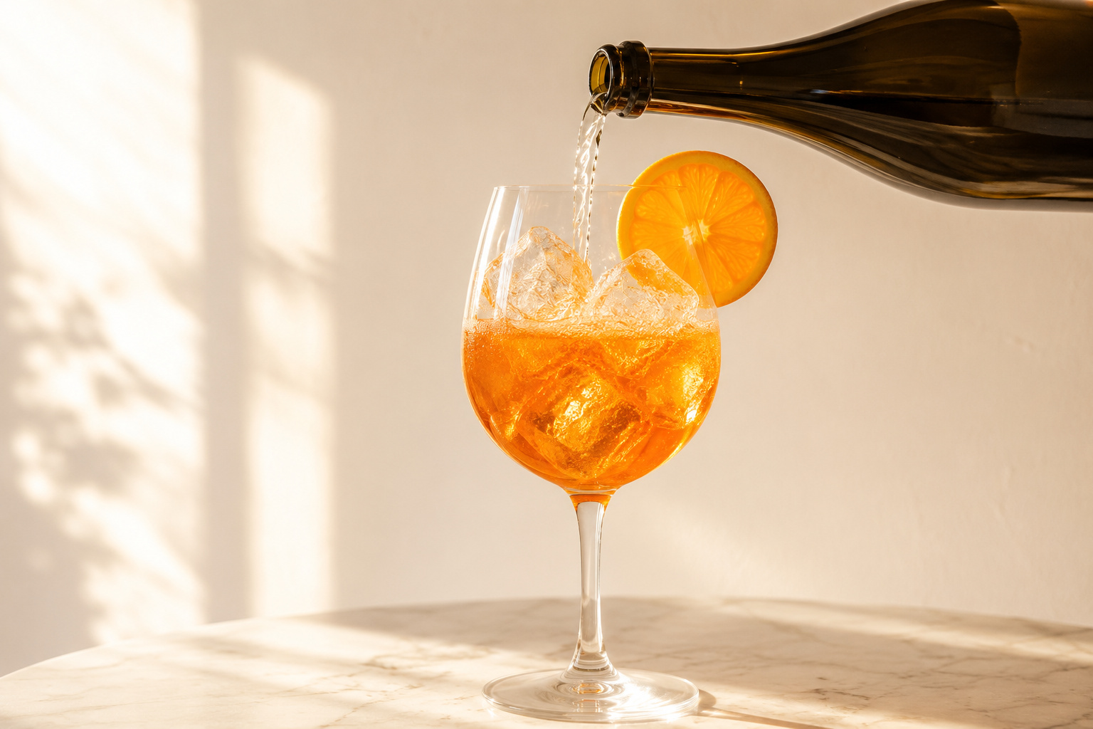 An Aperol Spritz being poured, Prosecco bottle mid-pour into a wine glass containing Aperol and ice