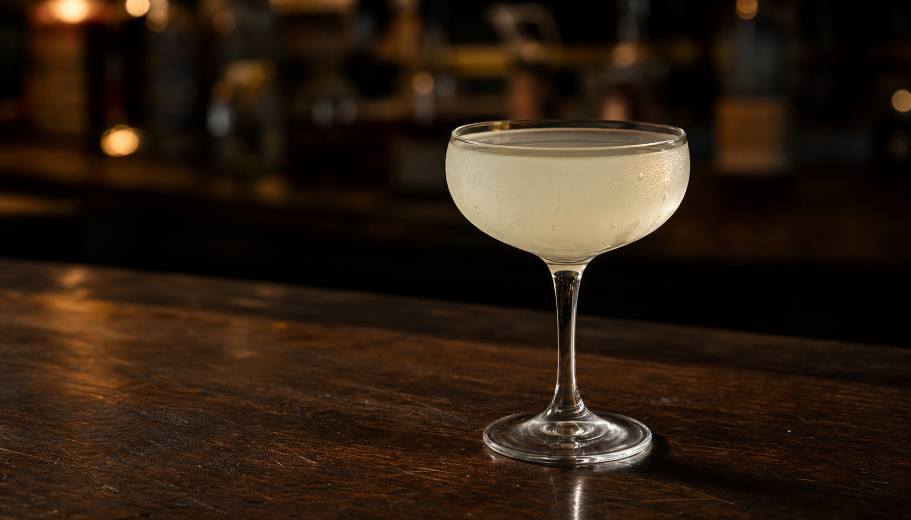 A classic daiquiri in a chilled coupe glass on a dark wood bar with warm low lighting