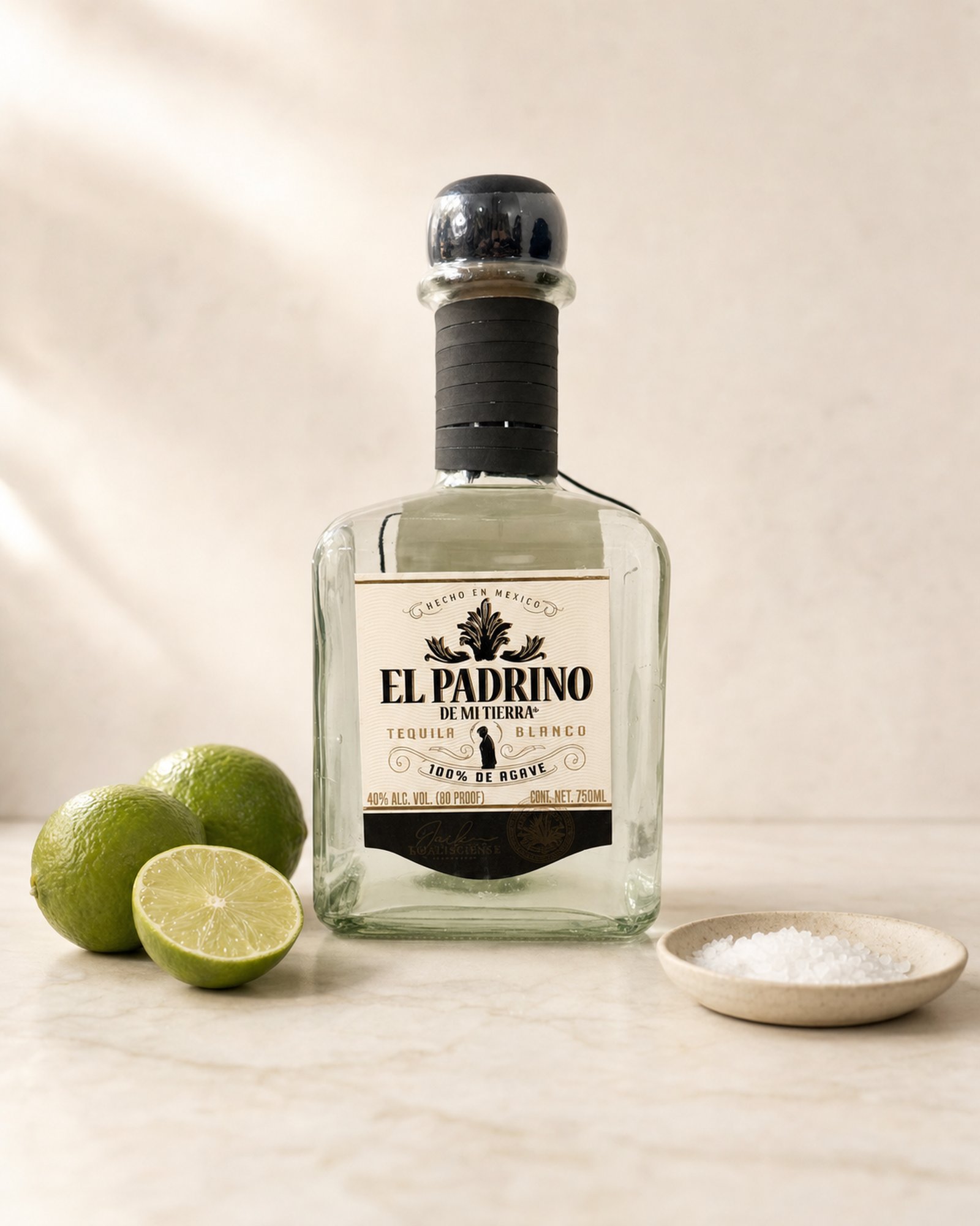 El Padrino Demitierra Blanco tequila bottle with fresh limes and a dish of coarse salt on marble