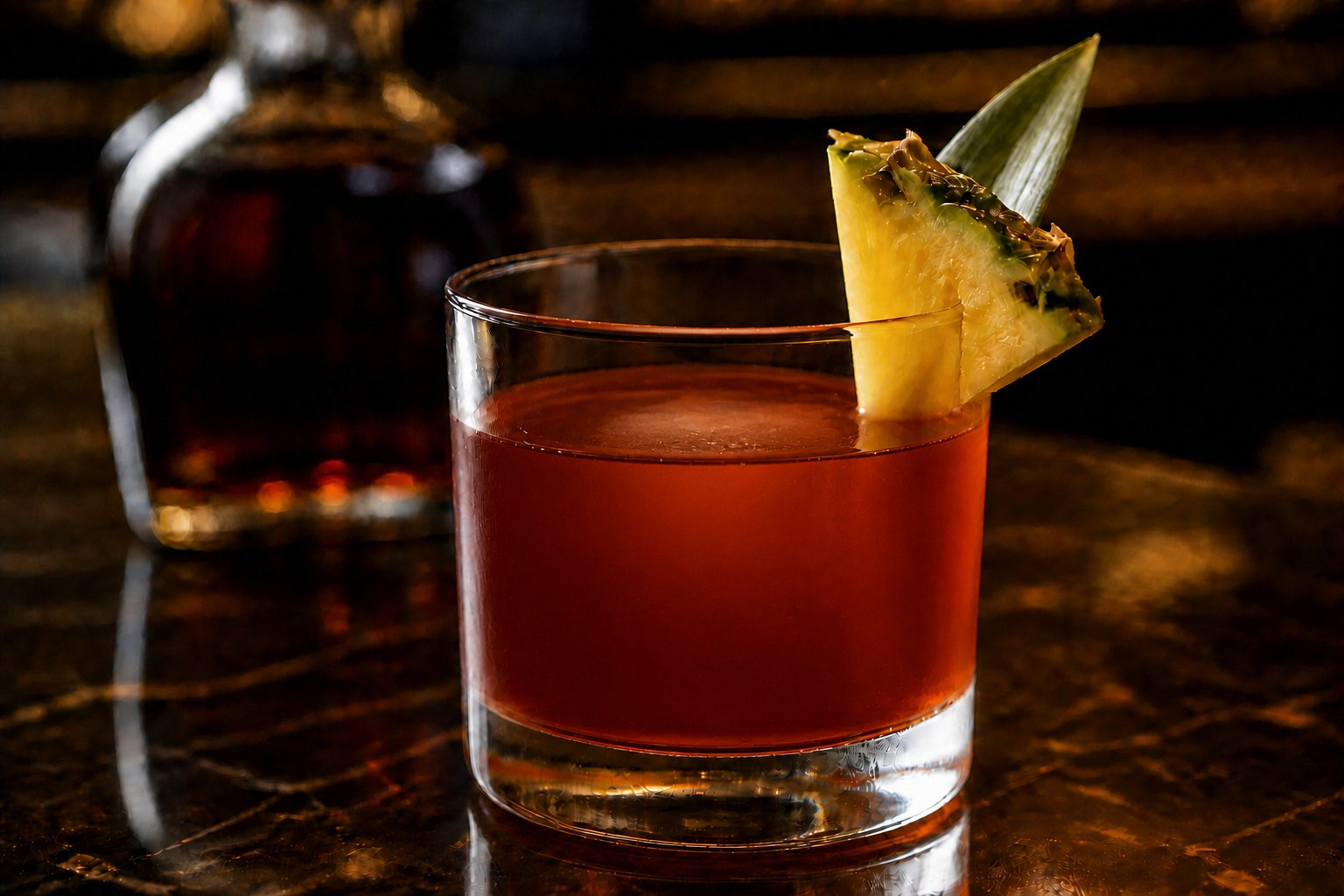 A Jungle Bird in a rocks glass, deep reddish-brown, garnished with a pineapple wedge and leaf